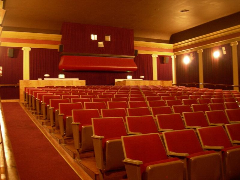 Sală de cinema cu scaune roșii și cortină în fața ecranului