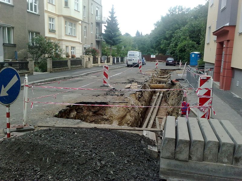 Stradă dintre blocuri săpată pentru lucrări la conducte, cu bandă de semnalizare